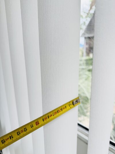 Maßband quer über eine weiße Lamelle eines Lamellenvorhangs gelegt, Messung zeigt rund 8,9 cm entsprechend 89 mm Lamellenbreite